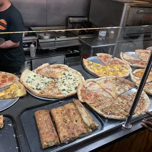 a man standing in front of a counter of pizzas