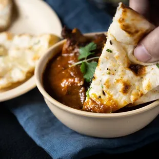 a hand holding a tortilla over a bowl of chili