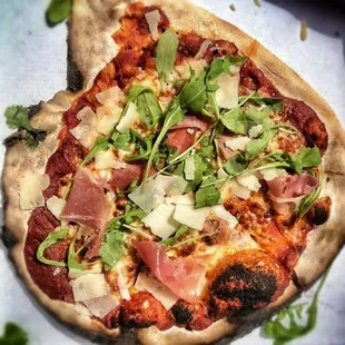 a pizza with ham, cheese, and arugula