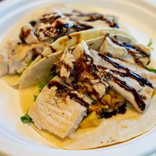 Mahi Tacos are served over mango salsa and drizzled with balsamic reduction.