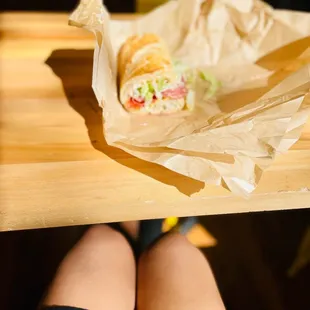 a person sitting at a table with a sandwich in a paper bag