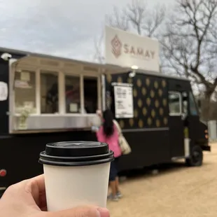a person holding a coffee cup in front of a food truck