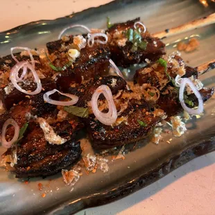 GRILLED PORK BELLY skewers with shaved shallots, Thai basil, and crispy fried garlic