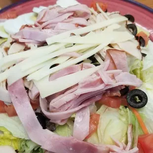 a salad with ham, lettuce, tomatoes, olives, and cheese