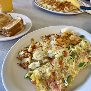 Front, Veggie omelette with hash browns and toast.  In background, eggs Benedict, hash browns, and juice.