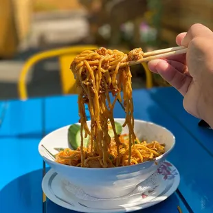 a person holding chopsticks over a bowl of noodles