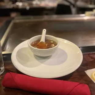 a bowl of soup on a white plate with a red napkin