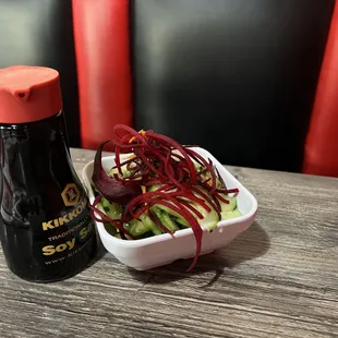a bowl of pickled cucumbers and a bottle of sauce