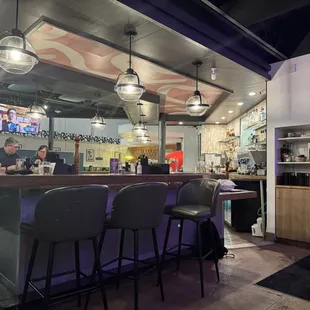 bar seating with loads of dirty dishes and cups on the counter and someone's personal backpack under the counter.