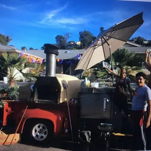 a man standing next to an outdoor pizza oven