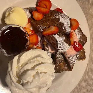 a plate of french toast with strawberries and whipped cream
