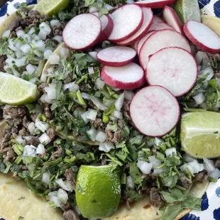a plate of tacos, limes, and radishes