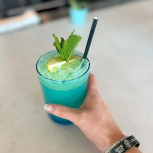 a hand holding a blue cocktail