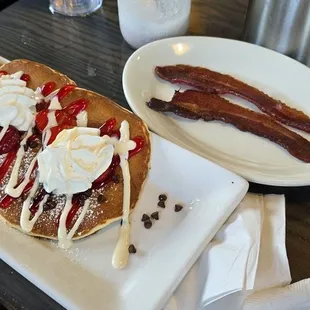 pancakes with chocolate chips and fresh strawberries, with a side of bacon