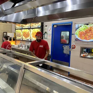 a man in a red shirt standing in a restaurant kitchen