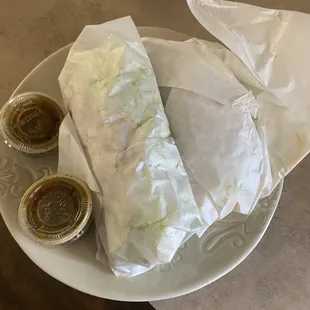 Two shredded beef tacos still wrapped  and two green salsas