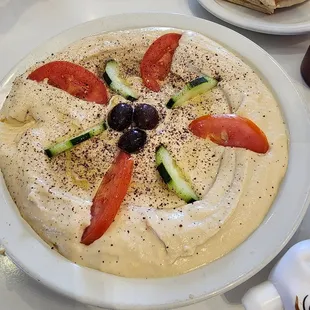 a plate of hummus, tomatoes, cucumbers, olives, and pita bread