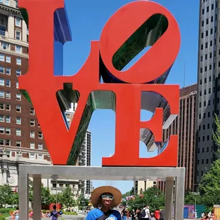 a man standing in front of a love sculpture