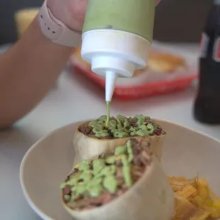 a person pouring guacamole on a burrito