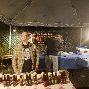 two men standing in front of a table of hot sauces