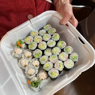 a person holding a container of sushi