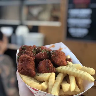 a hand holding a basket of fried chicken and french fries