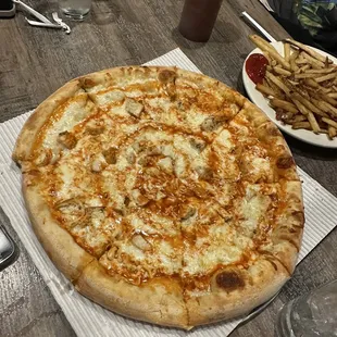 a pizza on a table with a plate of french fries