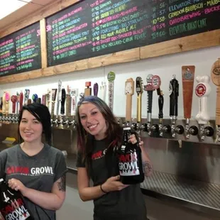 two women standing in front of a row of beer taps