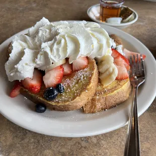 a plate of french toast with strawberries, bananas, and blueberries