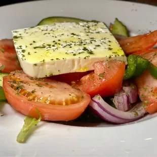 Greek salad with a bit of lettuce, lots of tomatoes, onions, cucumber and a slice of seasoned feta cheese.