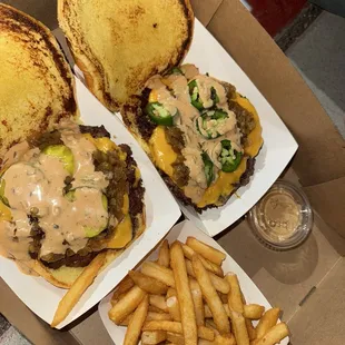 Two smash burgers, one with pickles and the other with jalapeños. Fries and sauce on the side.