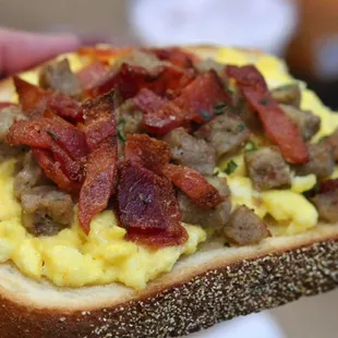 a person holding a sandwich with eggs and bacon