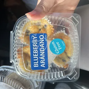 a hand holding a container of blueberry muffins