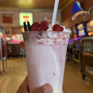a hand holding a cup of raspberry milkshake