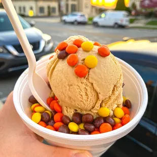 a hand holding a cup of ice cream with candy