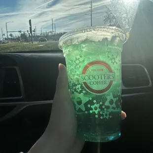 a hand holding a cup of green liquid