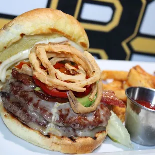 a burger with onion rings and a side of fries