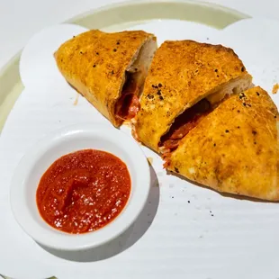 a piece of pizza on a plate with a small bowl of ketchup