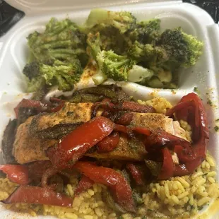 Salmon with yellow rice and broccoli also onions and bell peppers on the salmon