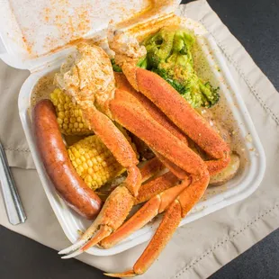 crab legs, corn and broccoli in a styrofoam container