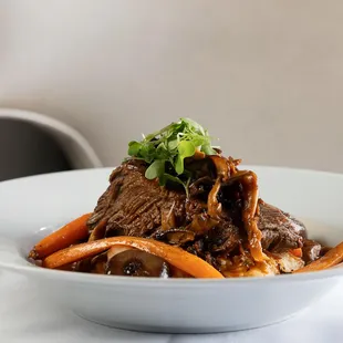 a plate of beef and carrots with a glass of wine