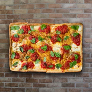 a square pizza with tomato sauce and basil leaves