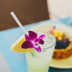a glass of lemonade with a purple flower and a slice of pineapple