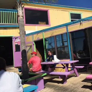people sitting at picnic tables in front of a colorful building