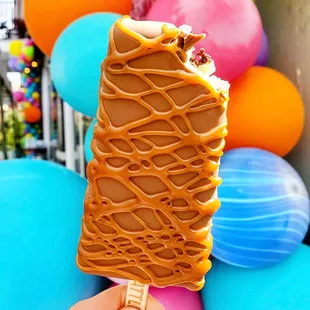 a hand holding an ice cream covered in caramel