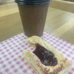 A cup of coffee with a raspberry pastry.