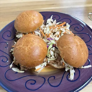 a purple plate with three pulled pork sandwiches and coleslaw slaw