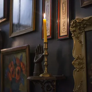 a candle on a table in front of a wall of framed pictures