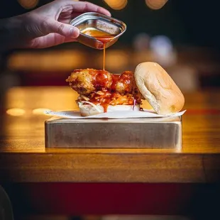 a person pouring sauce on a sandwich