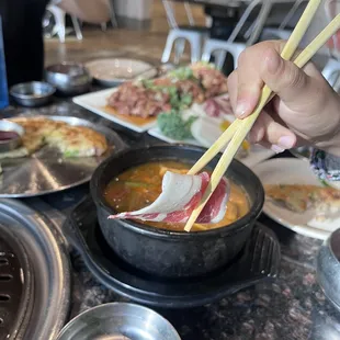 a person holding chopsticks over a bowl of soup